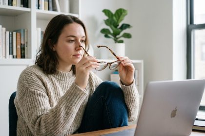 Jeune femme essayant des lunettes devant son ordinateur à la maison